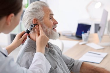 Duyma testi. Klinikte otoskopla hastaların kulaklarını muayene eden bir doktor. Metin için boşluk