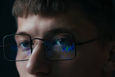 Siyah arka planda yansıması olan gözlüklü genç adam, yakın plan.