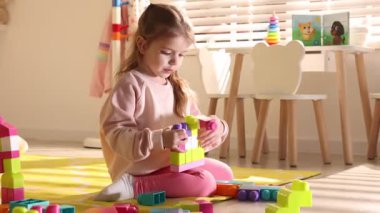 Oyun odasında yerde oyuncaklarla oynayan küçük bir kız. Kamera içeri giriyor.