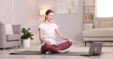 Hamile bir kadın evde dizüstü bilgisayarla yoga dersi alıyor.