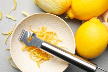 Taze limonlar, keyifli ve zester aletli gri masada, düz yerde.