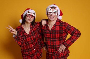 Noel Baba şapkalı mutlu çift, turuncu arka planda komik gözlükler ve pijamalar. Noel atmosferi