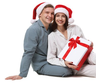 Noel Baba şapkalı ve pijamalı mutlu çift ve beyaz arka planda Noel hediyesi.