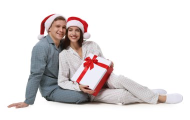 Noel Baba şapkalı ve pijamalı mutlu çift ve beyaz arka planda Noel hediyesi.