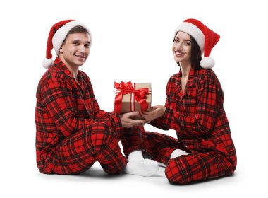 Noel Baba şapkalı ve pijamalı mutlu çift ve beyaz arka planda Noel hediyesi.