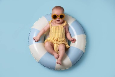 Şişirilebilir halkada güneş gözlüklü şirin bir bebek açık mavi arka planda, üst tarafta.