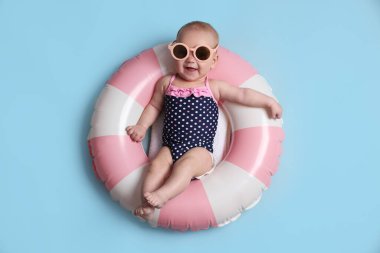 Şişirilebilir halkada güneş gözlüklü şirin bir bebek açık mavi arka planda, üst tarafta.