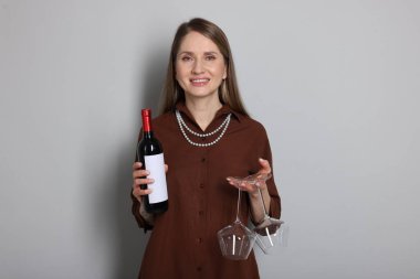 Açık gri arka planda bardakları ve bir şişe şarabı olan profesyonel şarap garsonu.