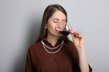 Profesyonel şarap garsonu açık gri arka planda şarap tadıyor.