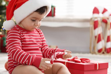 Noel Baba şapkalı küçük çocuk Noel için dekore edilmiş odada yerde hediyeyle