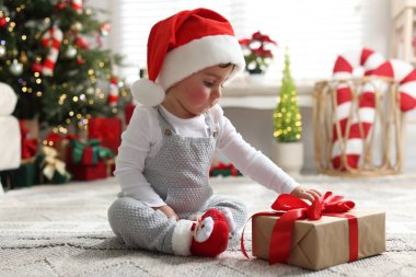 Noel Baba şapkalı küçük çocuk Noel için dekore edilmiş odada yerde hediyeyle