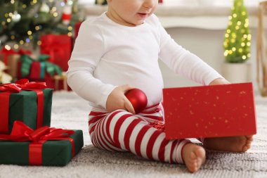 Noel için dekore edilmiş odada hediyeleri ve takıları olan küçük bir çocuk.