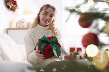 Evdeki koltukta Noel hediyesi ile gülümseyen kadın portresi. Bokeh etkisi