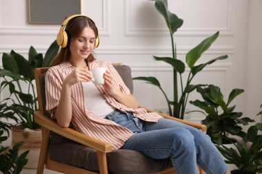 Elinde bir fincan aromatik kahve olan kadın evdeki koltukta müzik dinliyor. Metin için boşluk