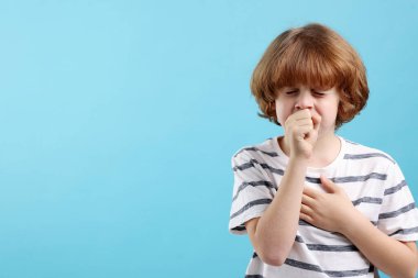 Küçük çocuk açık mavi arka planda öksürüyor, mesaj için yer var. Soğuk Semptom