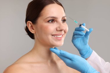 Estetik ameliyat. Doktor gri arka plandaki hastaya yüz enjeksiyonu yapıyor.