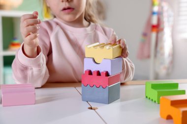 Oyun odasındaki beyaz masada oyuncaklarla oynayan mutlu küçük kız, yakın plan.