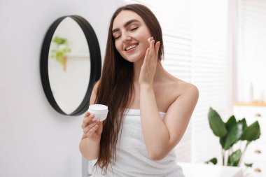 Havluya sarılı güzel bir kadın banyoda kozmetik ürünler uyguluyor.