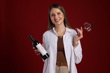 Kırmızı arka planda cam ve şarap şişesi olan profesyonel şarap garsonu.