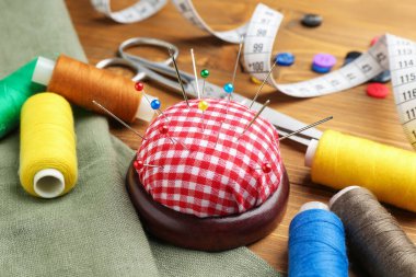 İğneler, iğneler, kumaşlar ve iplikçikler ile ahşap masada kareli iğnelik, yakın çekim