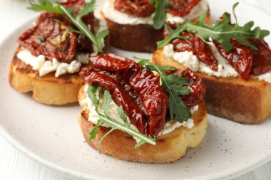 Krem peynirli lezzetli bruschettalar, güneşte kurutulmuş domatesler ve masanda roka, yakın plan.