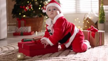 Noel Baba kostümlü şirin bir bebek. Evde Noel hediyeleri ve dekoru var.