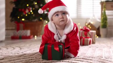 Noel Baba kostümlü şirin bir bebek ve evde yerde Noel hediyeleri.
