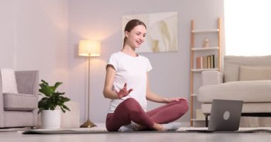 Hamile bir kadın evde dizüstü bilgisayarla yoga dersi alıyor.