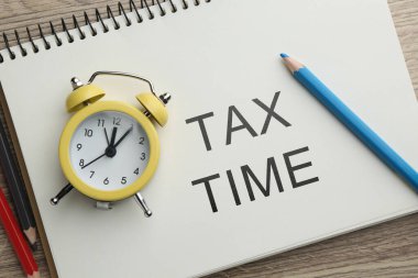 Vergi zamanı. Üzerinde yazı, alarm saati ve tahta masa üzerindeki kalemler olan defter, üst görünüm