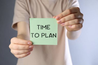 Plan yapma zamanı. Gri gradyan arkaplan üzerine yazılı kağıt nota tutan kadın, yakın plan