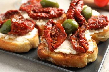 Krem peynirli lezzetli bruschettalar, güneşte kurutulmuş domatesler ve yeşil zeytinler masada, yakın plan.