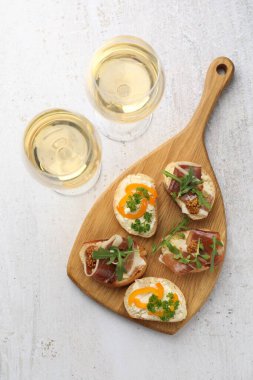 Beyaz masada servis edilen prosciutto ve şaraplı leziz bruschettalar, düz yerde.