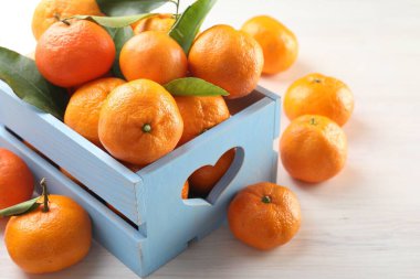 Taze mandalina ve yeşil yapraklar beyaz ahşap masada, yakın plan.