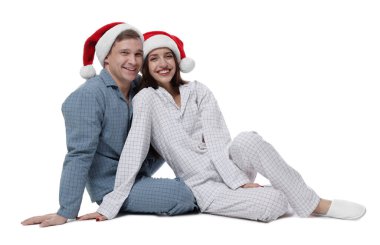 Beyaz arka planda Noel Baba şapkalı ve pijamalı mutlu bir çift. Noel atmosferi