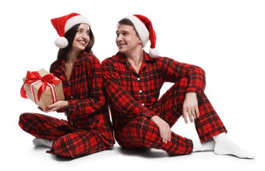 Noel Baba şapkalı ve pijamalı mutlu çift ve beyaz arka planda Noel hediyesi.