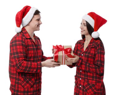 Noel Baba şapkalı ve pijamalı mutlu çift ve beyaz arka planda Noel hediyesi.