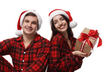 Noel Baba şapkalı ve pijamalı mutlu çift ve beyaz arka planda Noel hediyesi.