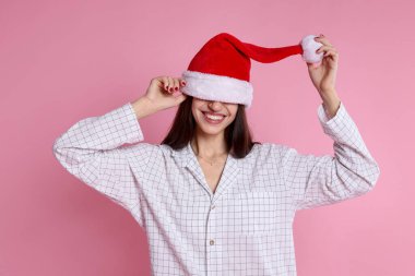 Pembe arka planda Noel Baba şapkalı ve pijamalı mutlu bir kadın. Noel atmosferi