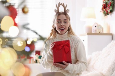Ren geyiği saç bandı takmış mutlu bir kadının portresi ve evdeki koltukta Noel hediyesi. Bokeh etkisi