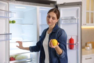 Mutfakta içi boş buzdolabının yanında limonlu bir kadın.