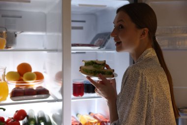 Açık buzdolabının yanında lezzetli sandviçleri olan bir kadın.