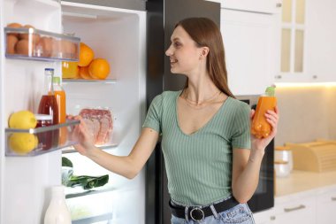 Mutfaktaki açık buzdolabının yanında portakal suyu şişesi olan kadın.
