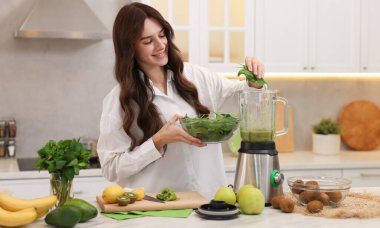 Gülümseyen kadın mutfaktaki beyaz mermer masada blender ile nefis smoothie yapıyor.
