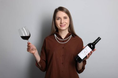 Açık gri arka planda cam ve bir şişe kırmızı şarap ile profesyonel şarap garsonu.