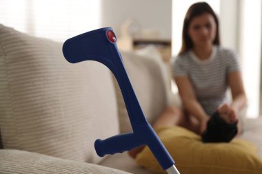 Evdeki koltukta bacağı ağrıyan kadın, dirsek değneğine odaklan.