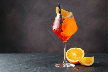 Bir bardak tazeleyici spritzer kokteyli ve siyah masada portakal dilimleri. Metin için boşluk