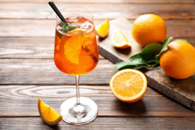 Bir bardak serinletici spritzer kokteyli ve portakallar ahşap masada.