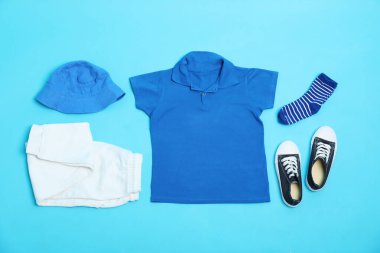 Açık mavi arka planda şık çocuk kıyafetleri ve ayakkabıları olan düz bir kompozisyon.