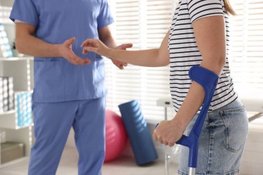 Fizyoterapist, klinikte terapi sırasında dirsek değneği olan bir kadına yardım ediyor.