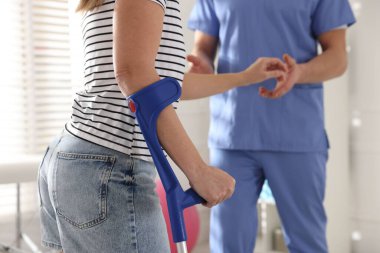 Fizyoterapist, klinikte terapi sırasında dirsek değneği olan bir kadına yardım ediyor.